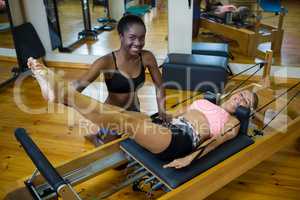 Smiling trainer assisting woman with pilates on reformer
