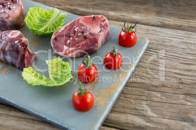 Sirloin steak, cherry tomatoes and cabbage leaves on board against wooden background