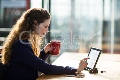 Businesswoman using digital table while having cup of coffee Businesswoman using digital table while having cup of coffee