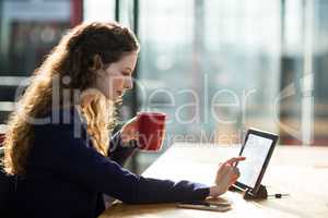 Businesswoman using digital table while having cup of coffee