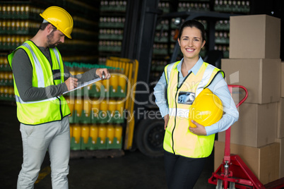 Female worker smiling at camera while coworker writing on clipboard