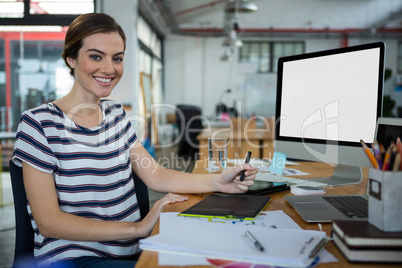 Smiling female graphic designer sitting at desk with graphic tablet and desktop on table