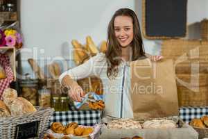 Portrait of smiling female staff putting croissant into a paper bag at counter