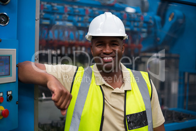 Portrait of smiling factory worker leaning on machine control cabinet