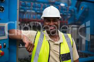 Portrait of smiling factory worker leaning on machine control cabinet