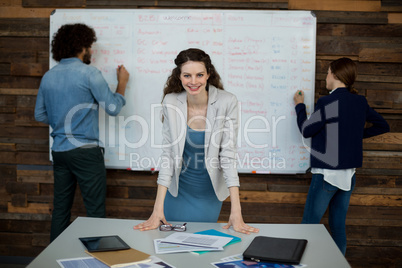 Portrait of smiling business executive leaning on table while colleague working in background