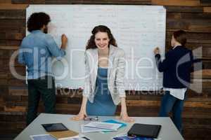 Portrait of smiling business executive leaning on table while colleague working in background