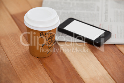 Close-up of disposable coffee cup, mobile phone and newspaper