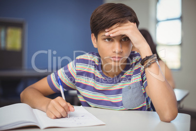 Tensed school boy doing homework in classroom