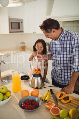 Father and daughter preparing smoothie in kitchen