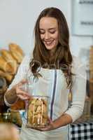 Smiling female staff holding a jar of cookies at counter