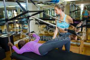 Trainer assisting woman with pilates on reformer