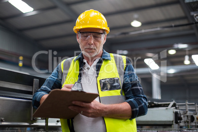 Male factory worker maintaining record on clipboard