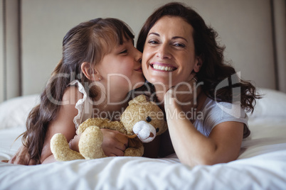 Daughter kissing her mother on cheek in bedroom