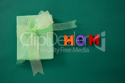 Gift box with alphabets displaying mom against green background