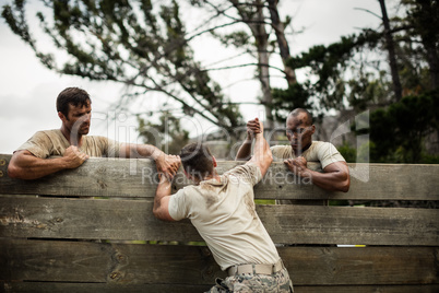 Soldiers helping man to climb wooden wall