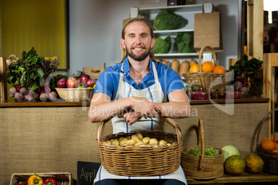 Smiling male staff siting with basket of potatoes at organic section