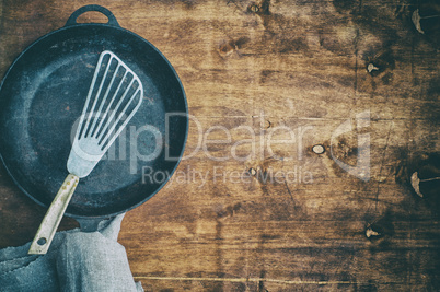 Black empty frying pan with an iron spatula on a brown wooden su