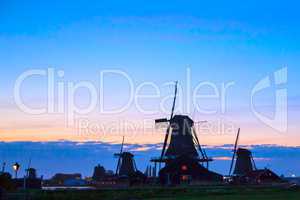 Silhouettes of Dutch mills near the lake at sunset
