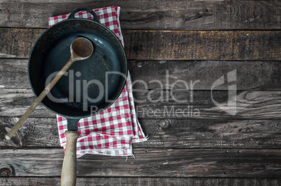 Black frying pan with a wooden spoon on a brown wooden surface