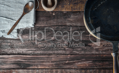 Brown wooden background with black frying pan and wooden spoon