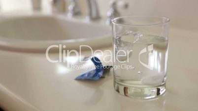 Slow Motion Effervescent Cold Tablets Dropping Into a Water Glass Near Bathroom Sink