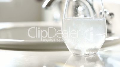 Slow Motion Effervescent Cold Tablets Dropping Into a Water Glass Near Bathroom Sink