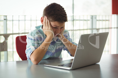 Sad schoolboy looking at laptop in library