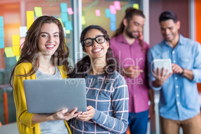 Two smiling female executives using laptop in office