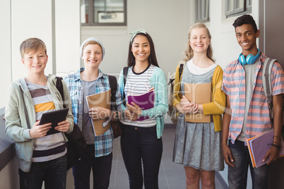 Portrait of smiling students standing with notebook and school bag in corridor