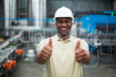 Happy factory worker showing his thumbs up in drinks production plant