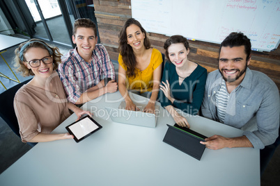 Smiling business executives sitting in office with digital tablet and laptop on table