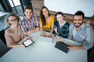 Smiling business executives sitting in office with digital tablet and laptop on table