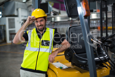Portrait of smiling factory worker leaning on forklift