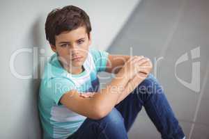 Portrait of sad schoolboy sitting in corridor