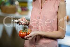 Woman using smartphone while holding tomatoes