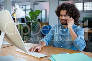 Graphic designer using computer while talking on mobile phone