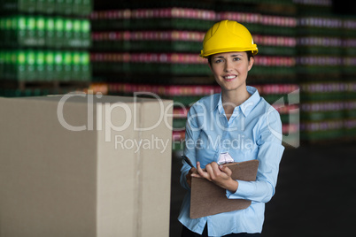 Female factory worker maintaining record on clipboard in factory