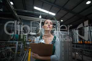 Female factory worker maintaining record on clipboard in factory