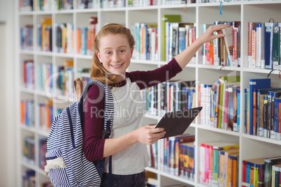 Portrait of happy schoolgirl selecting book in library