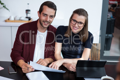 Smiling business executives discussing over digital tablet and document in meeting