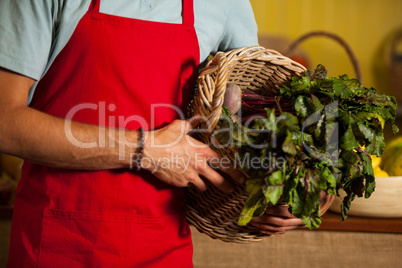 Mid section of male staff holding leafy vegetables in basket at organic section
