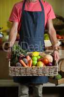 Mid section of male staff holding fresh vegetables in basket at organic section