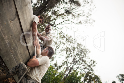 Soldiers helping man to climb wooden wall
