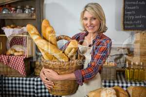 Smiling female staff holding wicker basket of french breads at counter