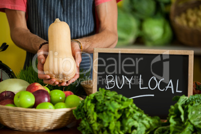 Mid section of male staff holding butternut squash with slate board in organic section