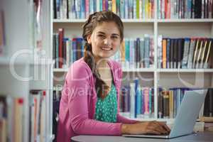 Portrait of happy schoolgirl using laptop in library