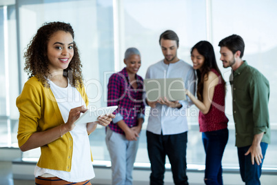 Woman using digital tablet in office while colleague discussing in background