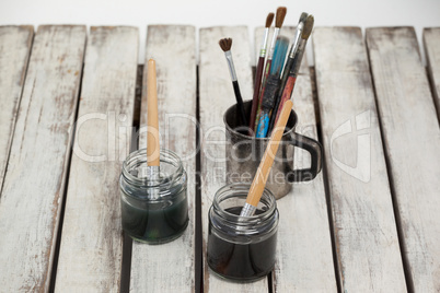 Jars of watercolor and paint brushes on wooden table