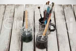 Jars of watercolor and paint brushes on wooden table